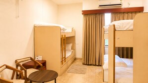 Une chambre d’hôtel avec des lits superposés, un bureau, des chaises, un appareil de climatisation et une fenêtre avec des rideaux.