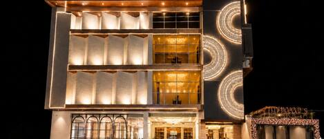 Ein mehrstöckiges Hotel mit modernem Design, das eine markante Eingangspforte mit Stufen und Pflanzenkübeln zeigt.