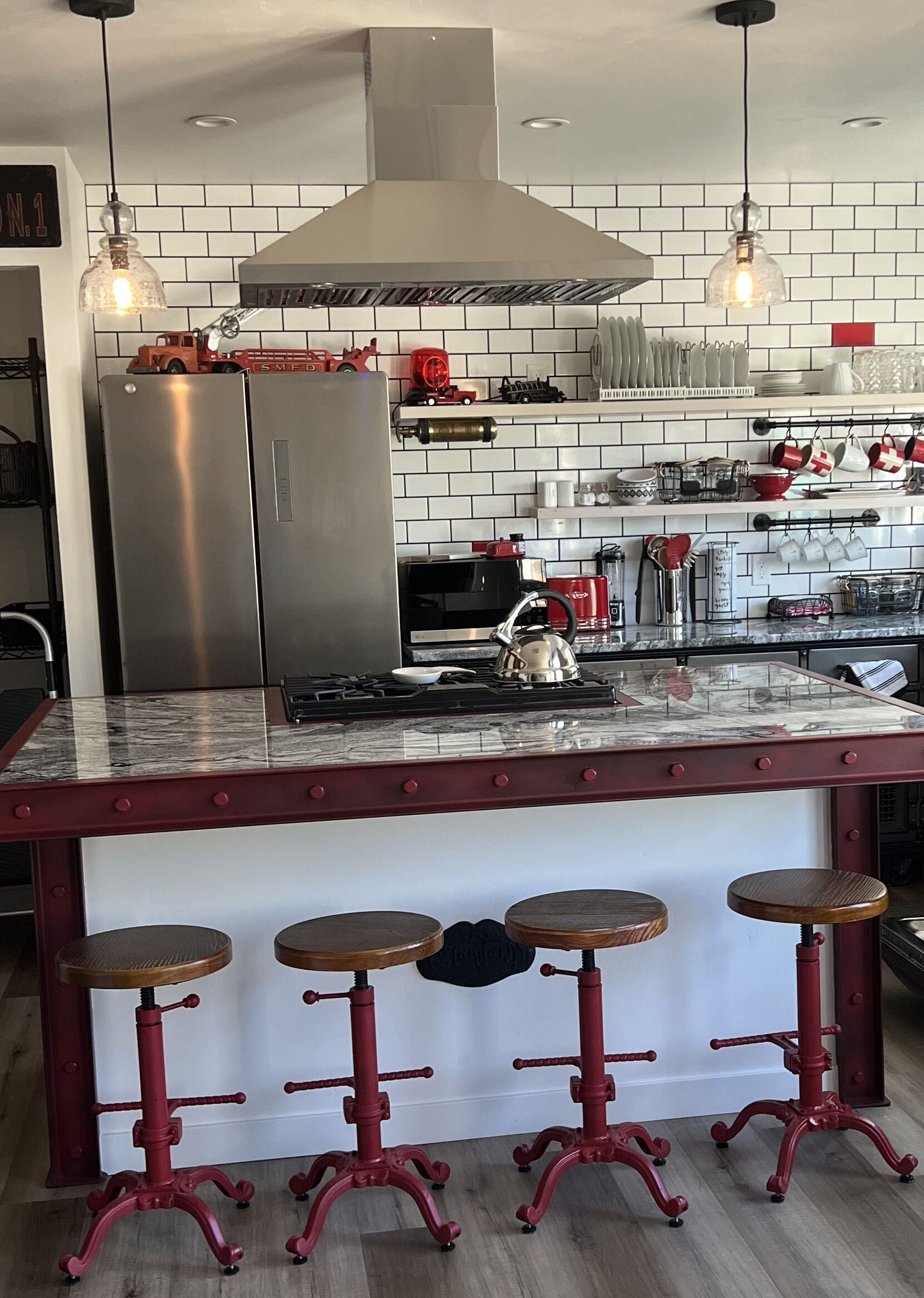 Une cuisine équipée d’un réfrigérateur en acier inoxydable, d’une cuisinière à gaz et d’un tabouret de bar rouge.
