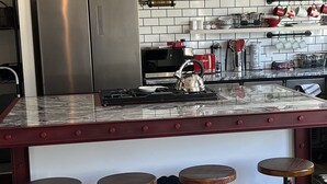 Een keuken met een roestvrijstalen koelkast, een gasfornuis en een rode barstoel.