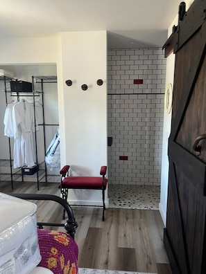 A room with a wooden floor, a red chair, a white wall with a brick pattern, a metal rack with white robes, and a wooden wardrobe.