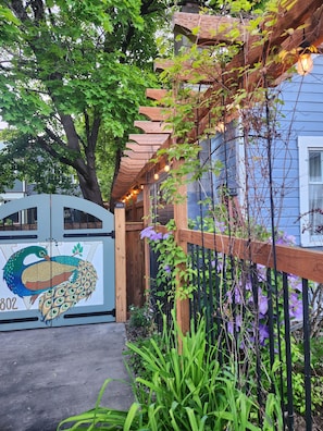A residential property with a wooden pergola, a peacock mural, and a garden with purple flowers.