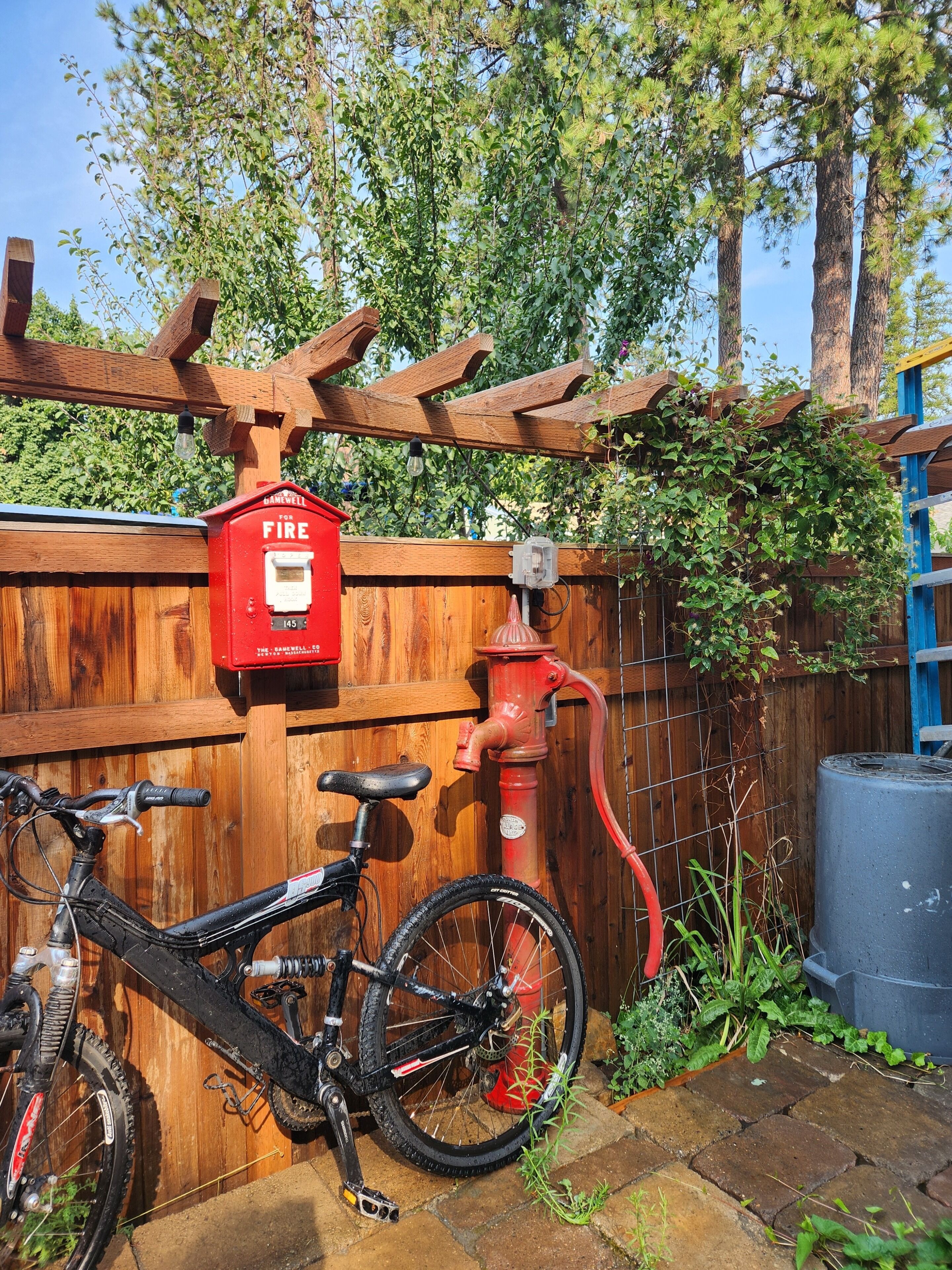A wooden fence with a red fire hydrant, a bicycle, and a wooden pergola.
