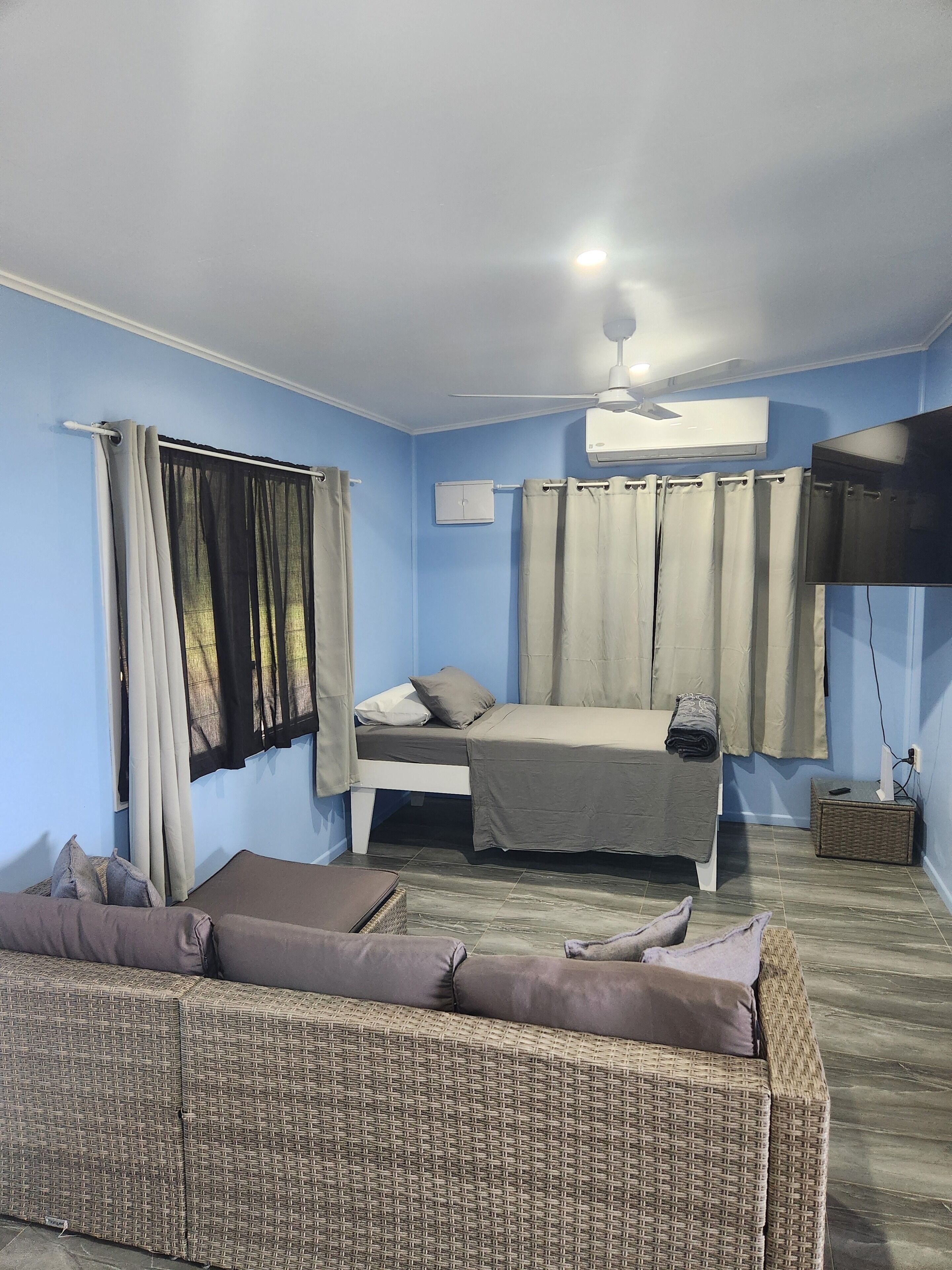 A room with a bed, a sofa, a ceiling fan, and a TV.