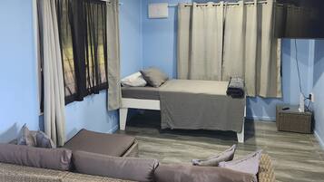 A room with a bed, a sofa, a ceiling fan, and a TV.