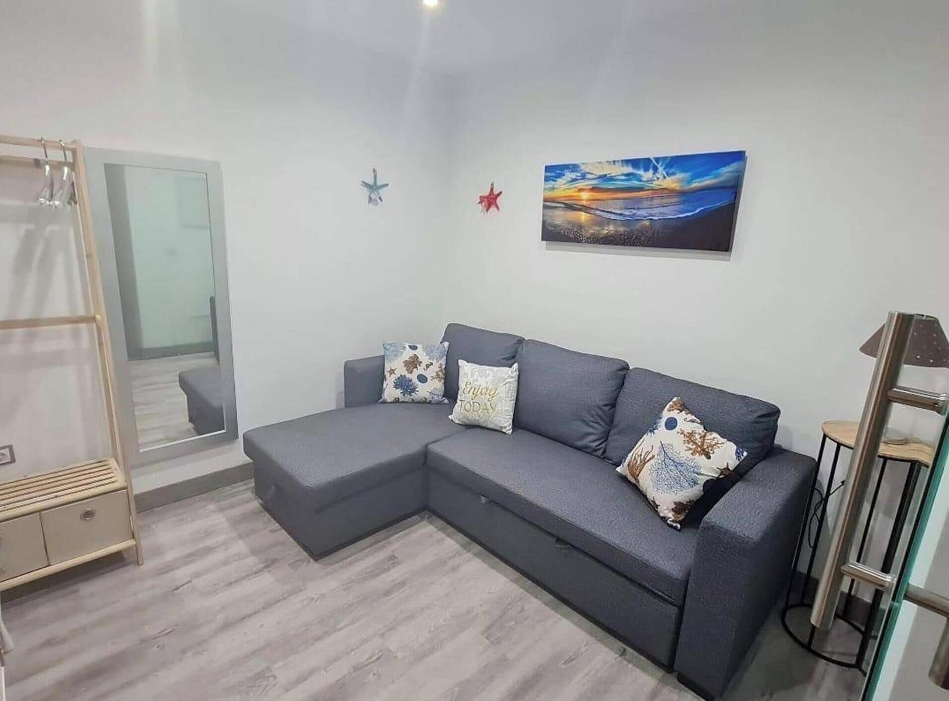 Uma sala de estar moderna com um sofá seccional cinza, uma porta de vidro que dá para uma varanda e um quadro com um pôr do sol na parede.