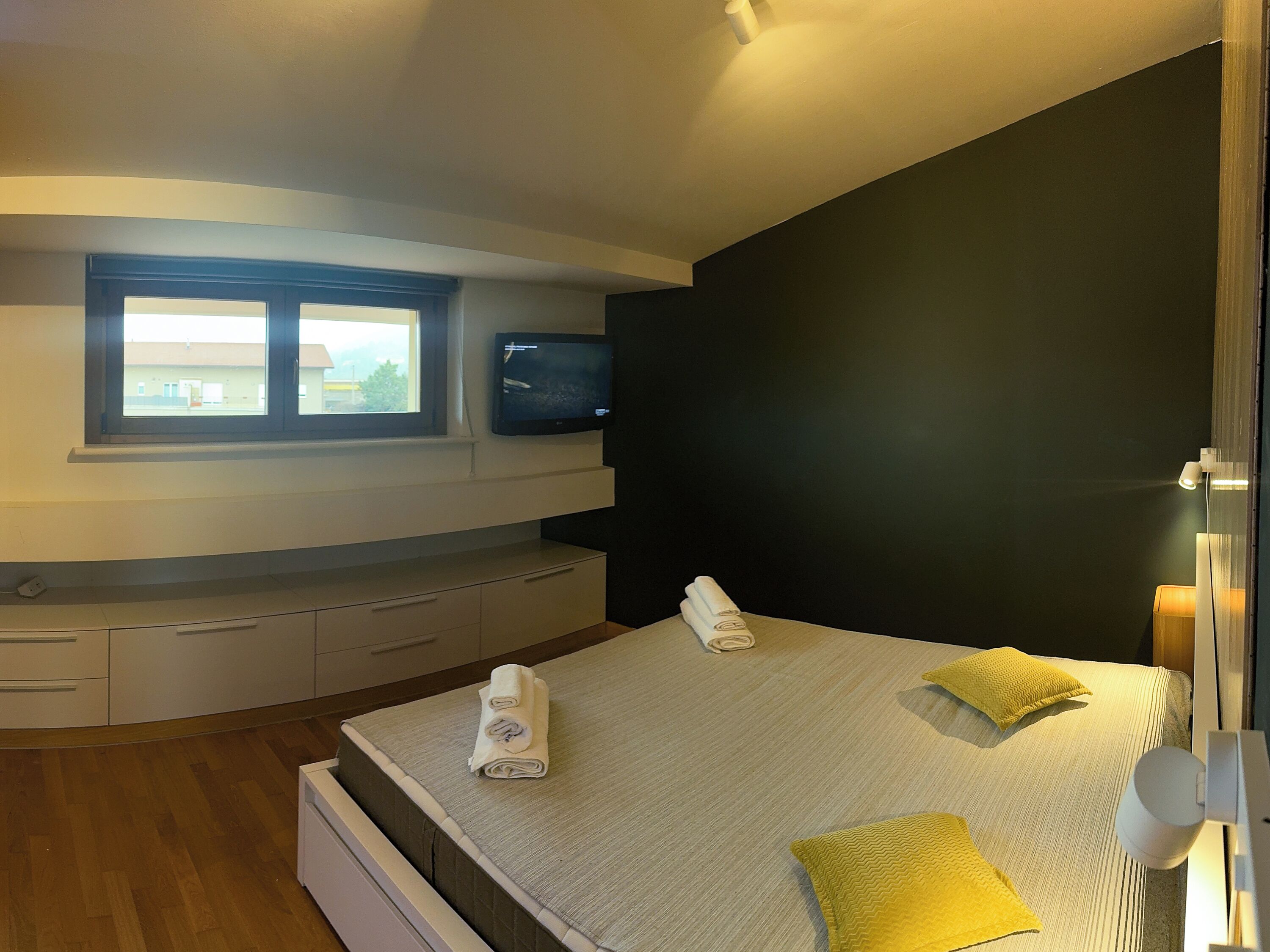 A modern bedroom with a bed, a TV, a window, and a bedside table.