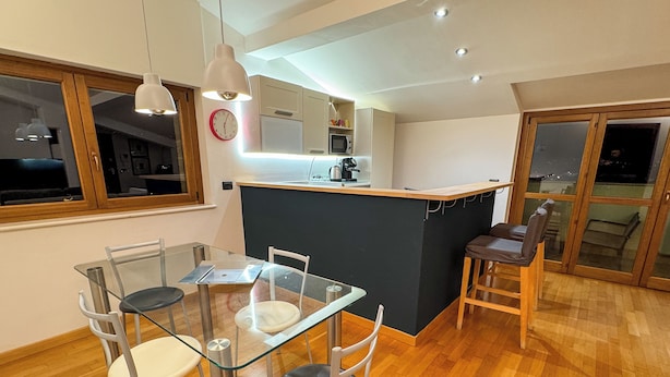 Una cocina moderna con una isla central, un área de comedor con una mesa y sillas de vidrio, y vistas al exterior a través de una puerta corrediza.