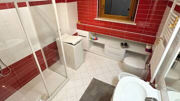 A bathroom with a glass shower enclosure, a white sink, a toilet, and a red-tiled wall.