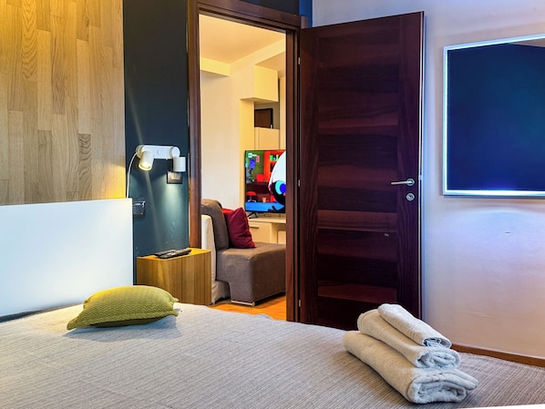 A hotel room with a bed, a TV, a wooden door, and a wall-mounted TV.