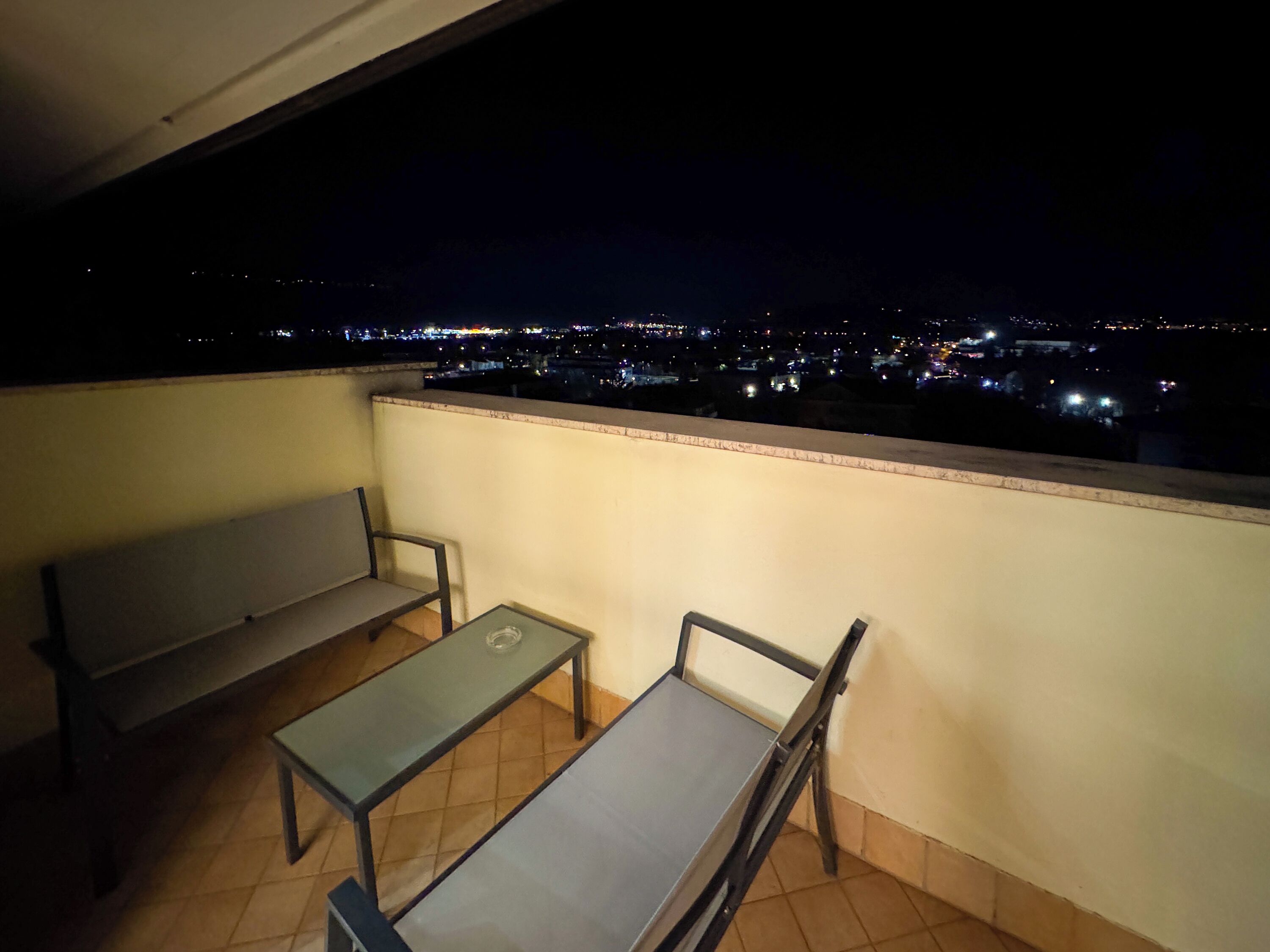 Un balcon avec un banc et une table, donnant sur une vue panoramique de la ville la nuit.