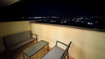 Un balcon avec un banc et une table, donnant sur une vue panoramique de la ville la nuit.