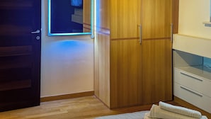 Una habitación con un armario de madera, un espejo con luz y un mueble blanco.