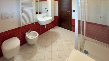 Ein Badezimmer mit Toilette, Bidet, Waschbecken und Duschbereich.