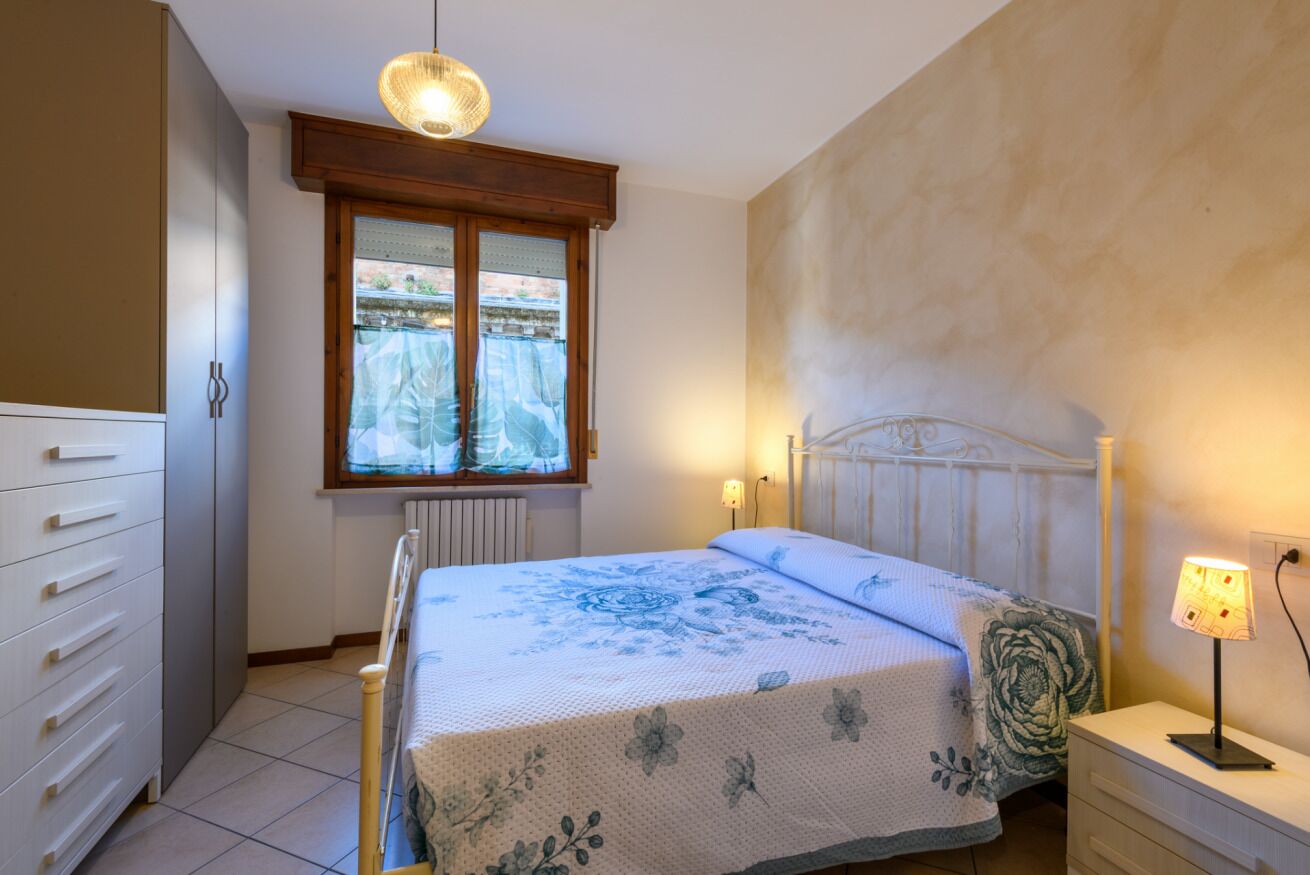 Ein Schlafzimmer mit Bett, Nachttisch, Schminktisch, einem Fenster mit Blick und einer Wandlampe.