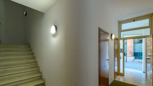 Eine Treppe führt zu einer Tür mit Glastür, einem Wandleuchte und einem gefliesten Boden.
