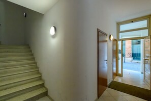 Eine Treppe führt zu einer Tür mit Glastür, einem Wandleuchte und einem gefliesten Boden.