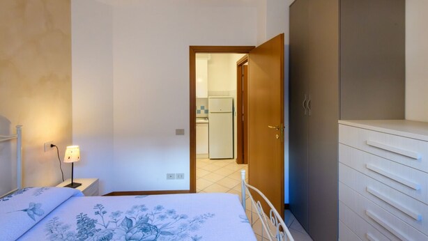 Ein Schlafzimmer mit Bett, Nachttisch, Lampe, Kleiderschrank und einer Tür zum Badezimmer.