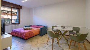 Ein kleines Zimmer mit einem Bett, einem Tisch mit Stühlen, einem Fenster und einer Heizung.