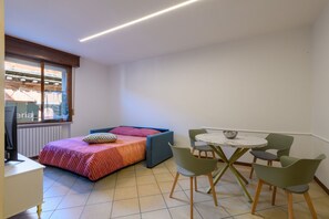 Ein kleines Zimmer mit einem Bett, einem Tisch mit Stühlen, einem Fenster und einer Heizung.