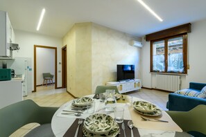 Ein Essbereich mit einem Tisch für vier Personen, einem Fernseher und einem Fenster mit Jalousien.