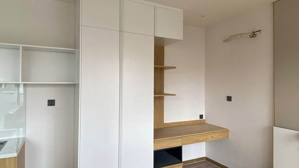 A room with a built-in white cabinet, a wooden shelf unit, and a small black object on the wall. - DaNy Living Thao Dien by DNM Hospitality (Ho Chi Minh City)