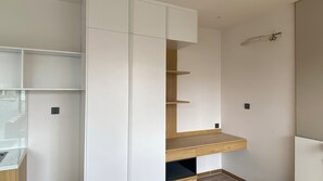A room with a built-in white cabinet, a wooden shelf unit, and a small black object on the wall. - DaNy Living Thao Dien by DNM Hospitality (Ho Chi Minh City)