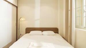 A neatly made bed with pillows, a bedside lamp, and a window with curtains. - DaNy Living Thao Dien by DNM Hospitality (Ho Chi Minh City)