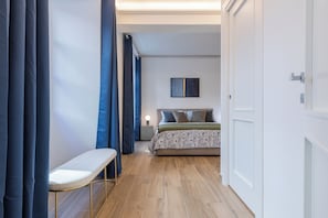 Un pasillo estrecho que conduce a un dormitorio con una cama, una mesita de noche y una lámpara fijada a la pared.