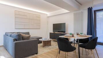 Una sala moderna con un sofá gris, una mesa de centro, una mesa de comedor con sillas, un televisor de pantalla plana y una gran obra de arte abstracto en la pared.