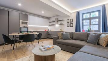 Una sala de estar moderna con un sofá gris, sillas negras, una mesa de centro y una cocina al fondo.
