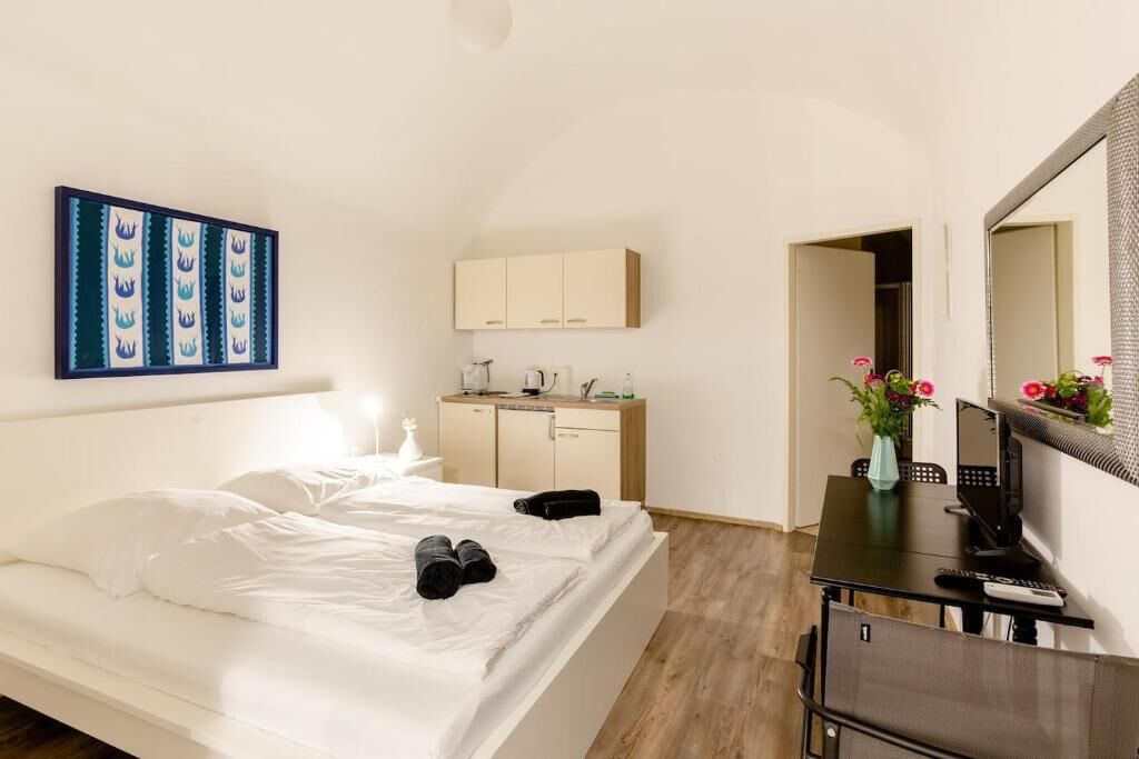 A hotel room with a bed, a desk, a mirror, a wardrobe, and a painting on the wall.