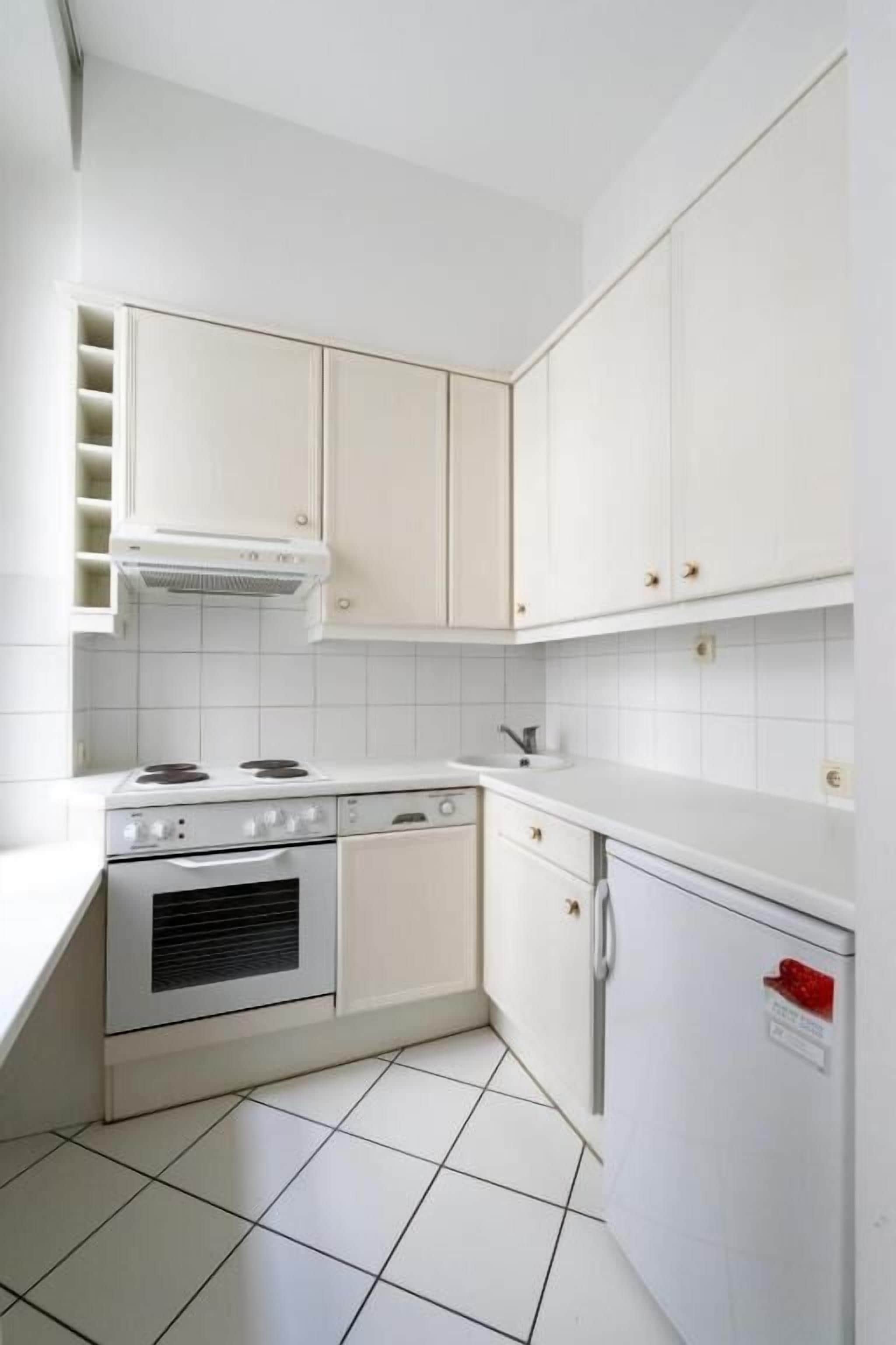 Eine kleine Küche mit weißen Schränken, einem Herd und einem Kühlschrank.