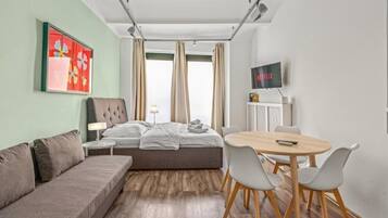 Ein modernes Hotelzimmer mit einem Bett, einem Sofa, einem Esstisch mit Stühlen, einem Fernseher und einem Fenster mit Vorhängen.