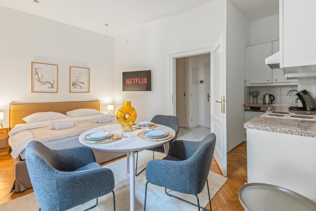 A modern hotel room with a bed, bedside table, and a small dining area with a table and chairs.