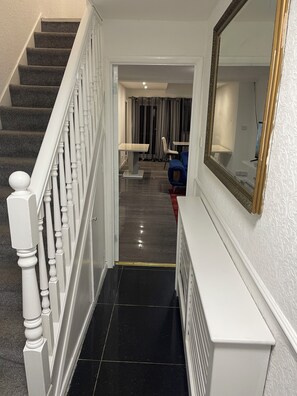 A staircase with white balusters leading to a landing, a black tiled floor, and a mirror on the wall. - Elites Apartment – Spacious 4-Bedroom Home with Free Parking (London)