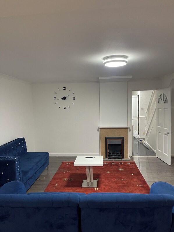 A living room with a blue sofa, a white table, and a fireplace. - Elites Apartment – Spacious 4-Bedroom Home with Free Parking (London)