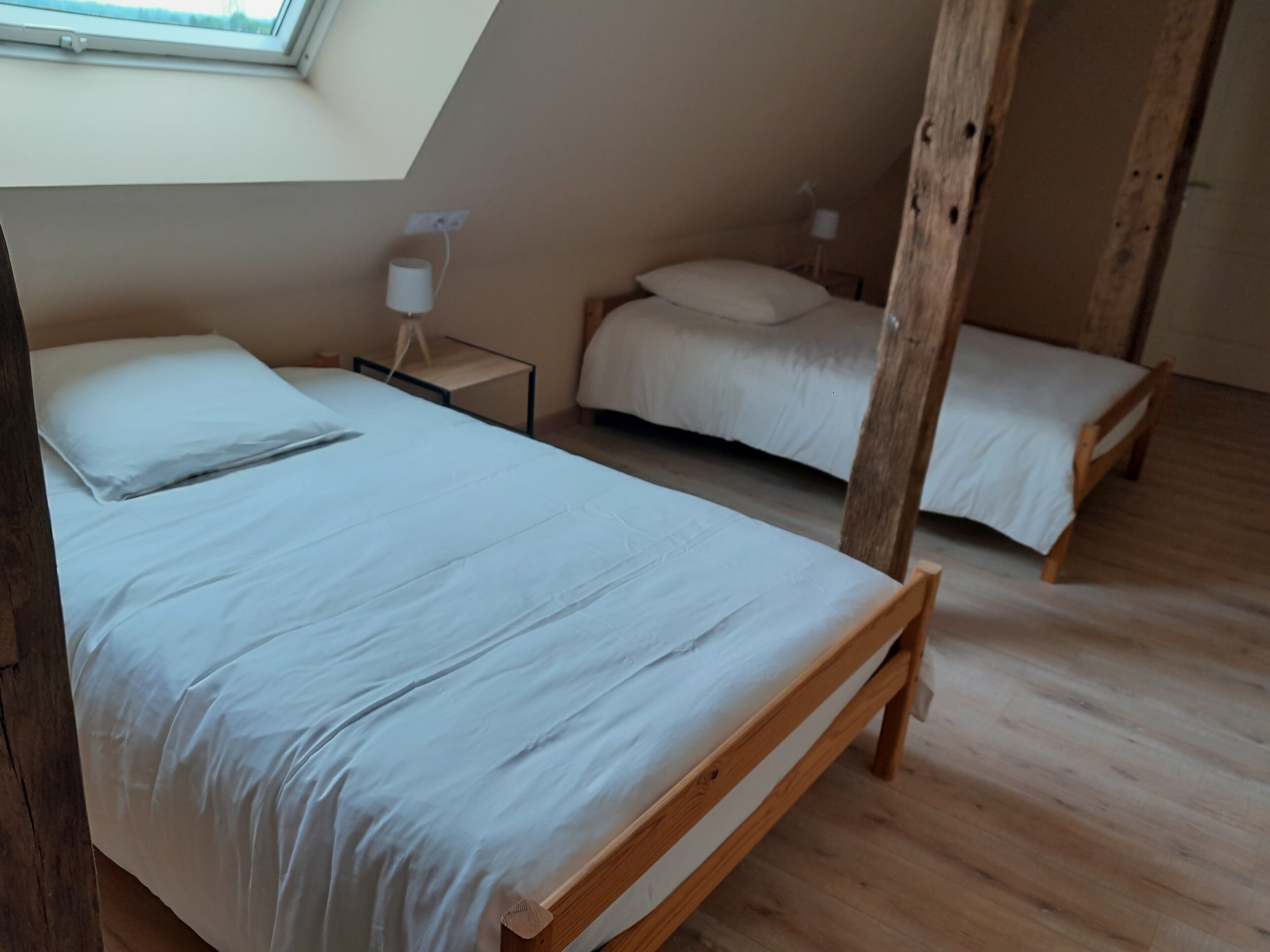 Une chambre avec deux lits en bois, une table de chevet avec une lampe et une lucarne.