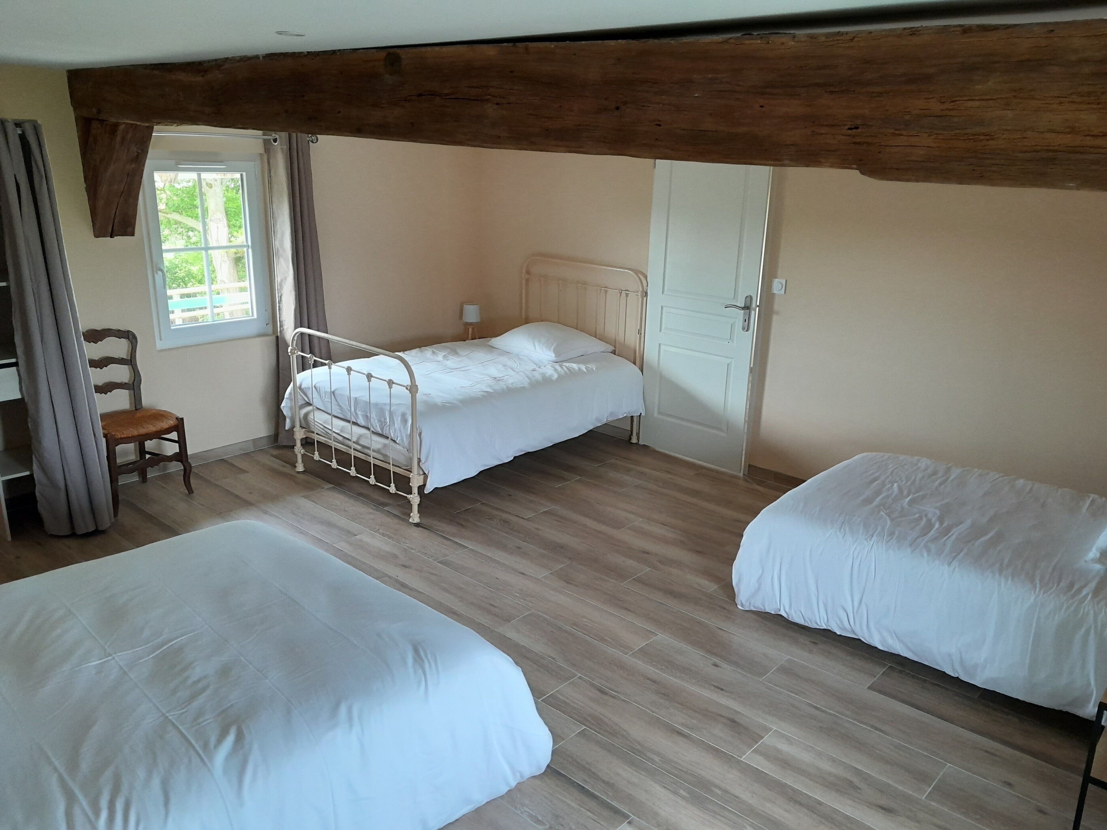 Une chambre avec deux lits, une chaise, une fenêtre avec des rideaux et une porte.