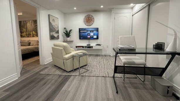 A modern living room with a sofa, a glass table, a TV, and a clock on the wall.