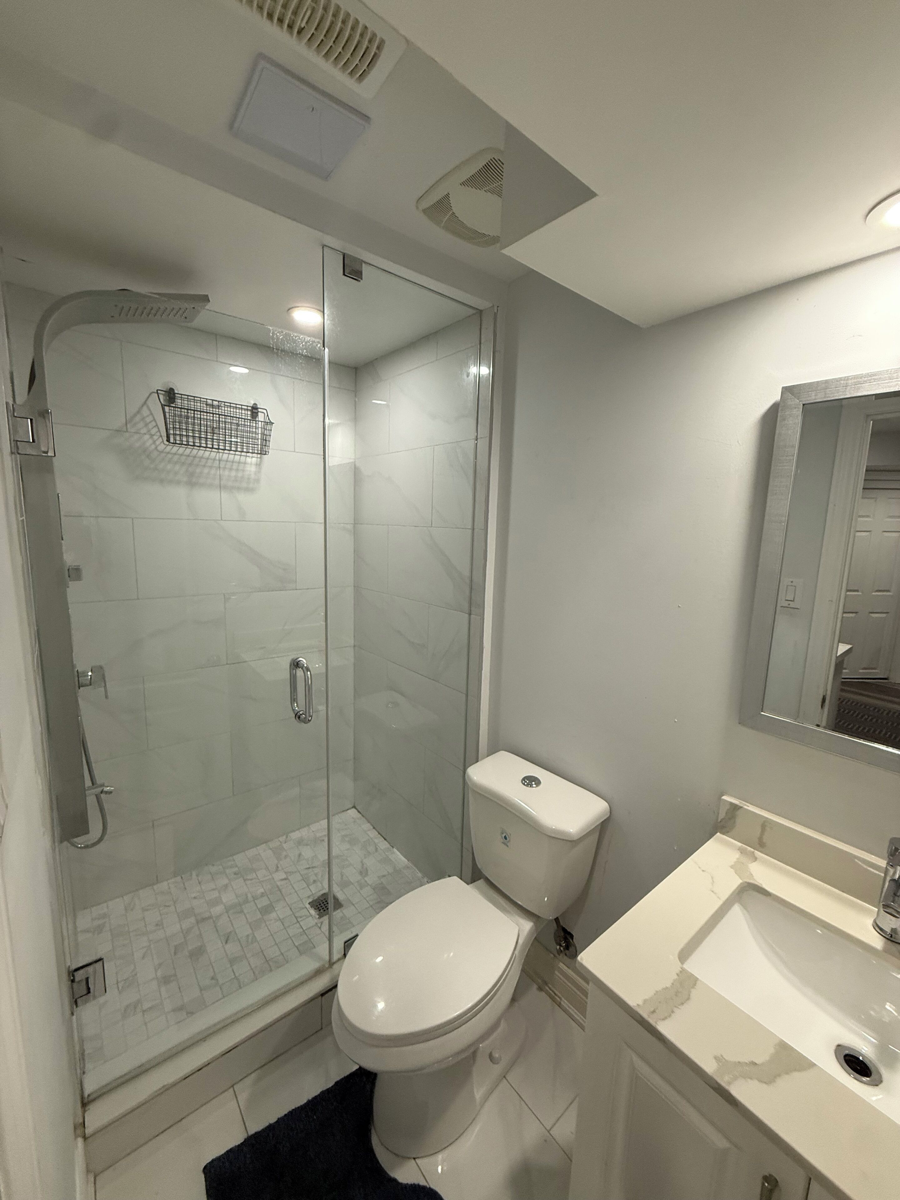 A bathroom with a glass-enclosed shower, a toilet, and a sink.