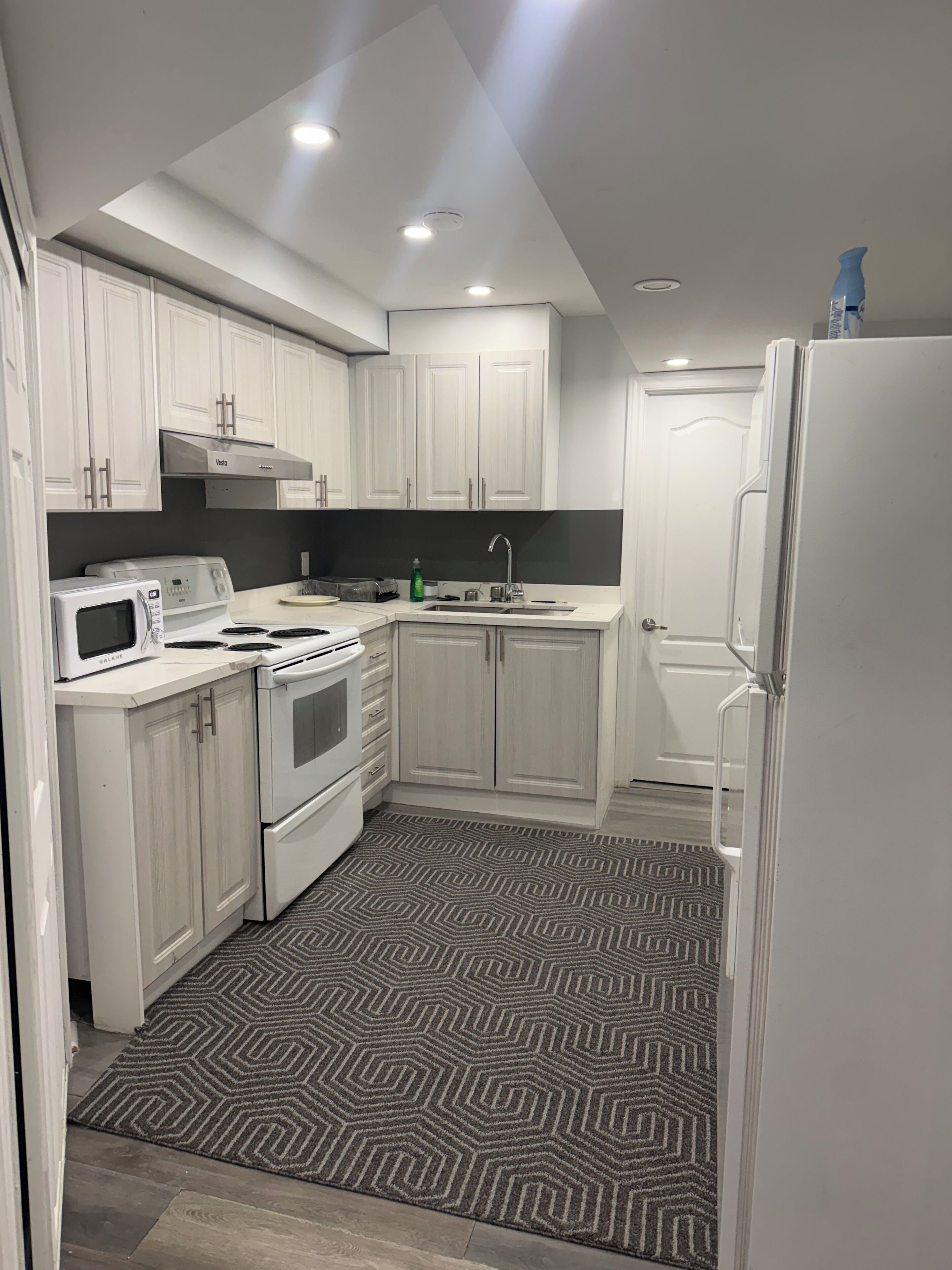 A compact kitchen with white cabinetry, a microwave, a stove, and a refrigerator.