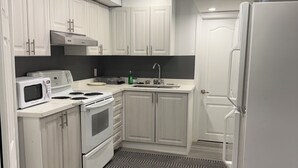 A compact kitchen with white cabinetry, a microwave, a stove, and a refrigerator.