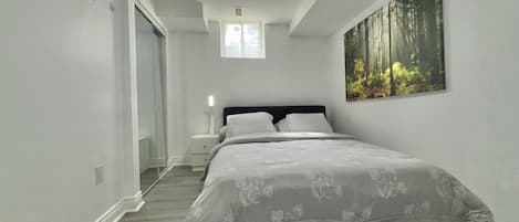 A bedroom with a bed, a nightstand, a painting, and a ceiling light.