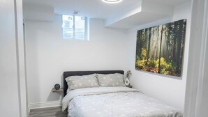 A bedroom with a bed, a nightstand, a wall-mounted painting, and a window.