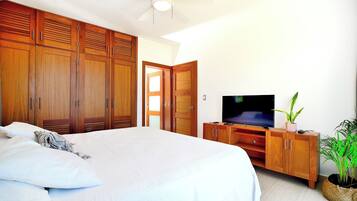 A bedroom with a large bed, wooden wardrobe, a television on a wooden stand, and a potted plant.
