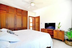 Ein Schlafzimmer mit einem großen Bett, einem Holzschrank, einem Fernseher auf einem Holztisch und einer Zimmerpflanze.