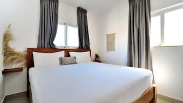 A bedroom with a large bed, two windows with curtains, a ceiling fan, and a wall-mounted macrame piece.