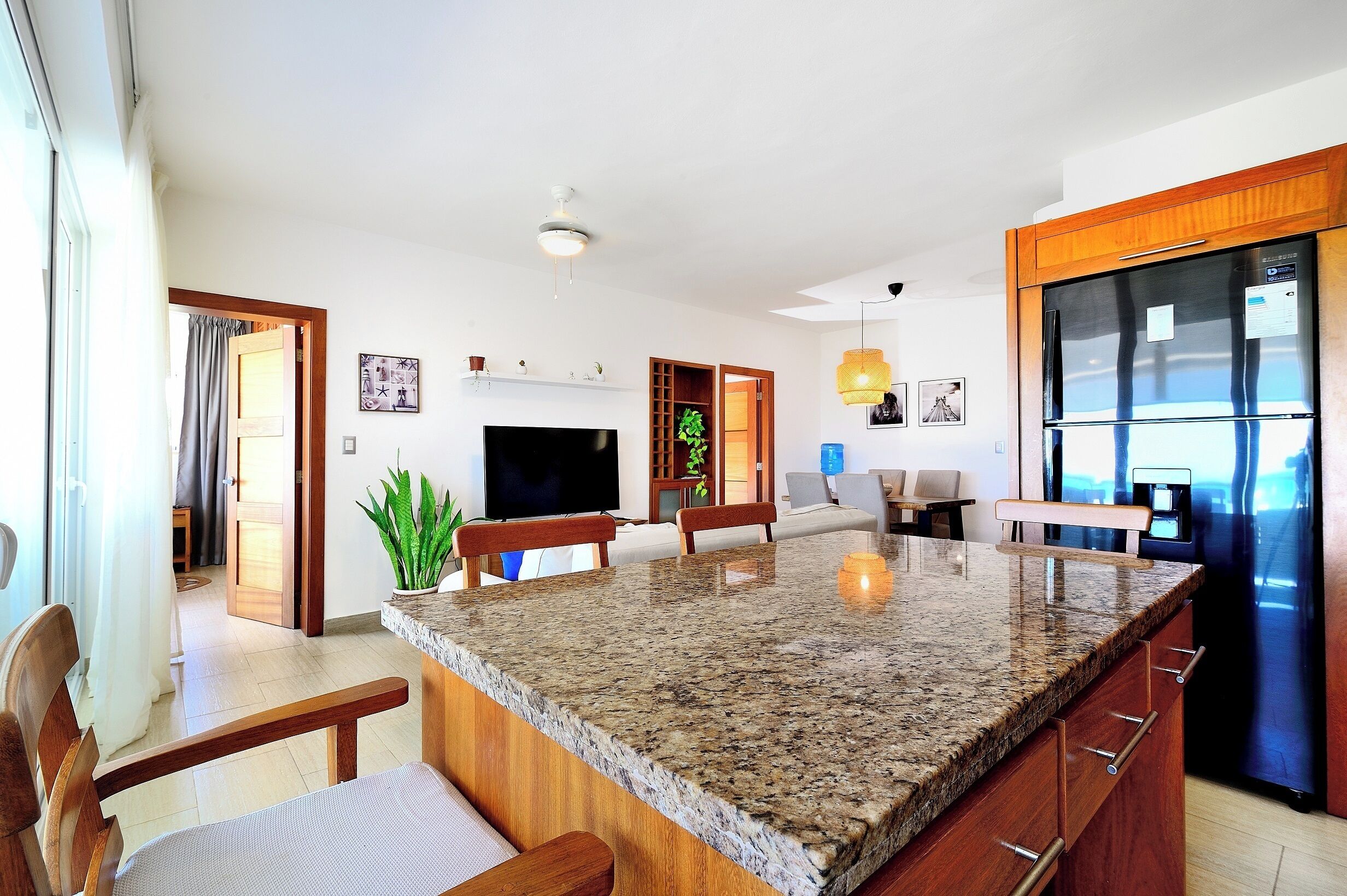 A modern kitchen with a granite countertop, wooden cabinets, a built-in refrigerator, and a dining area with chairs and a table.