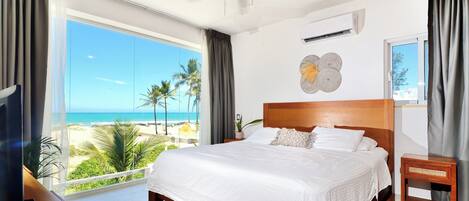 Une chambre d’hôtel avec un grand lit, un ventilateur de plafond, une télévision et vue sur la plage.